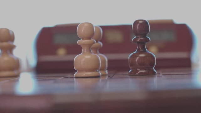 Two focused players are engaged in an intense game of chess. The camera captures a detailed close-up of a hand strategically moving a pawn across the wooden board.