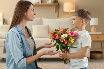 Mother's Day. Happy woman with her son and bouquet of flowers at home