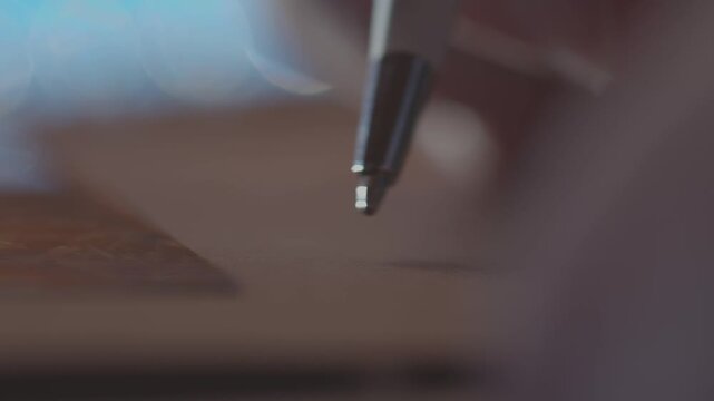 A captivating macro shot shows a ballpoint pen writing on paper in a spiral notebook. The shallow depth of field creates beautiful bokeh lights in the blurred background
