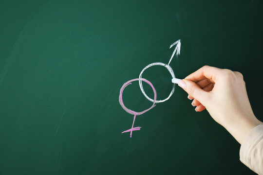Sex Education. Woman drawing gender symbols on green chalkboard, closeup. Space for text
