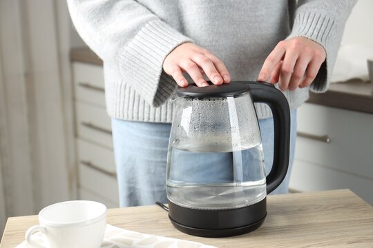 Woman with electric kettle at wooden table indoors, closeup