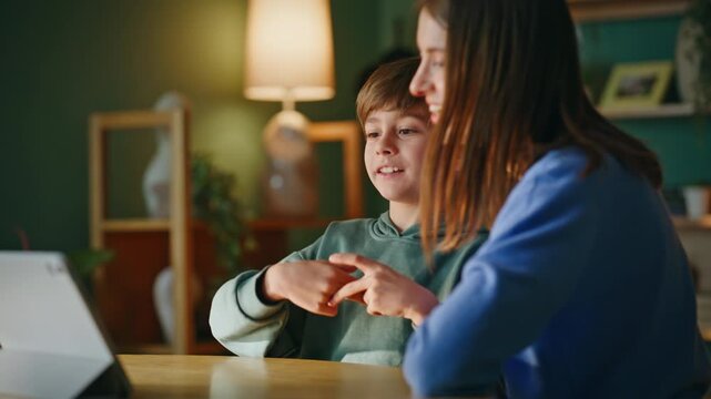 Mother son enjoy tablet game sitting home desk together closeup. Smiling mom boy