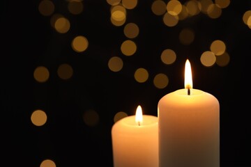 Burning candles against black background with blurred lights, closeup. Space for text