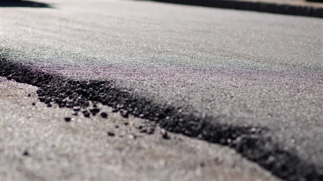 Close up view of freshly laid asphalt texture on road surface during street construction, with road roller moving in the background.