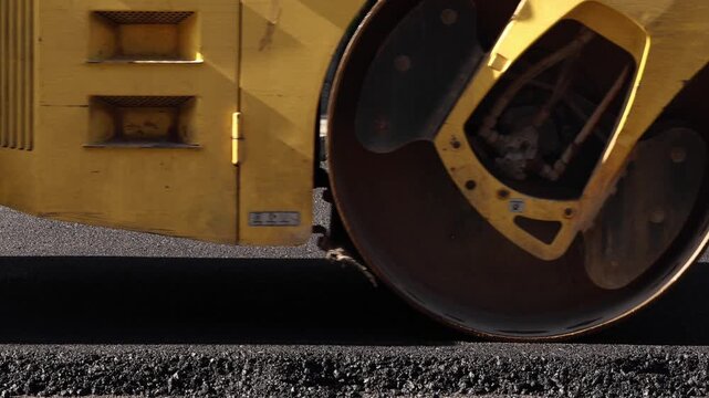 Steam roller compacting freshly laid asphalt on urban street during road construction and resurfacing work.