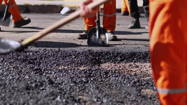 Construction workers using shovels to spread and level fresh asphalt during street paving and road repair work.