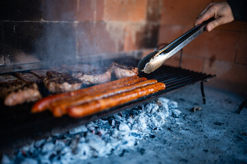 Naklejka premium Hand grilling meat and sausages on hot charcoal