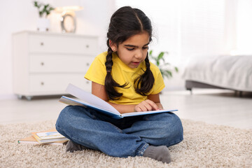 Fototapeta premium Cute little girl reading book on floor at home