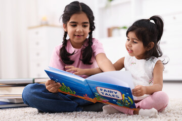Fototapeta premium Cute little girls reading book together at home