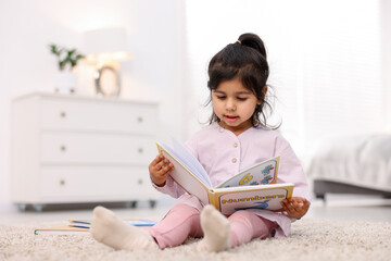 Fototapeta premium Cute little girl reading book on floor at home. Space for text