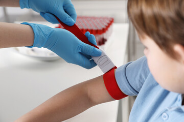 Nurse putting medical tourniquet on little boy's arm in clinic, closeup