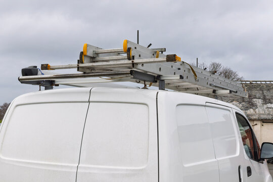 Extension ladder secured to roof rack of white contractor work van