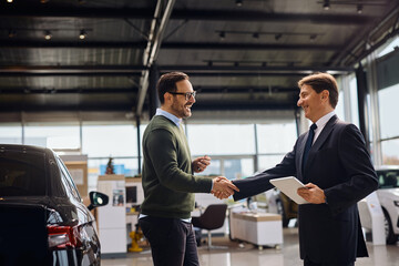 Happy man shaking hands with salesman after buying new car in auto salon. © Drazen
