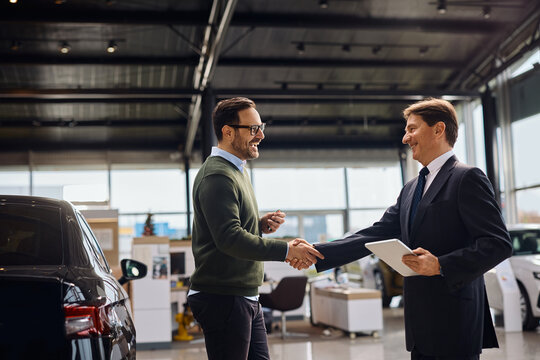 Happy man shaking hands with salesman after buying new car in auto salon.