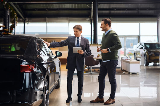 Mature salesman talking to customer at car dealership.