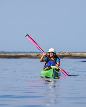 Front view of a female kayaker in a green boat using a pink paddle and wearing a safety helmet and life jacket.