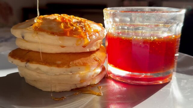 A close-up shot of golden syrup being poured over a stack of fluffy pancakes. This appetizing breakfast scene with honey dripping is perfect for food, cooking, and dessert content.