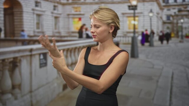 Woman signing with hands near face on street by stone balustrade wearing black tanktop; focused communication.