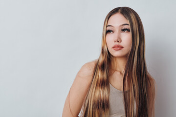 Naklejka premium Woman with long hair and makeup posing against light background, portrait of young female model with straight hair and natural expression in studio photography.