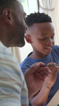 Vertical video: Painting son in blue tee and dad in striped polo offering brush, crafting at home