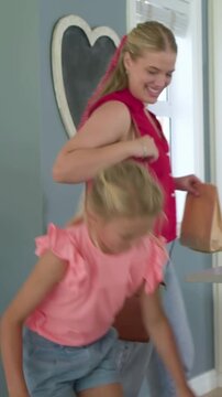 Daughter entering with grocery bags and unpacking, mother handing mesh bag, storing food on island