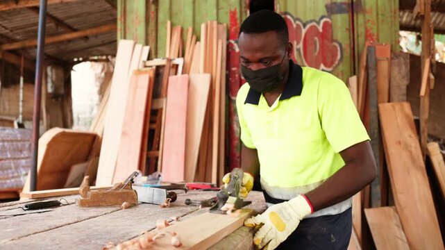 Local African male carpenter using a metal hand plane to smooth a wooden plank in his workshop
