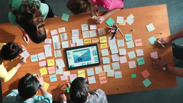 Top down view of programmer brainstorming and planning about web design while looking at tablet wireframe prototype. Aerial view of skilled developer team talking about digital application. Symposium.
