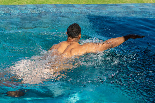 Swimmer is propelling forward through turquoise pool water near coping with sunlight reflections