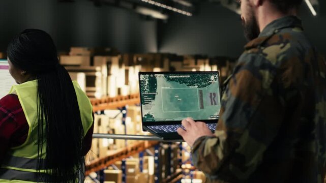 Male army officer does military surveillance using drone monitoring software inside a warehouse storage center. Personnel ensuring defense operations, mission tactical planning.