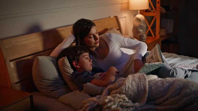Mother read bedtime story adorable son lying together evening bedroom closeup. 