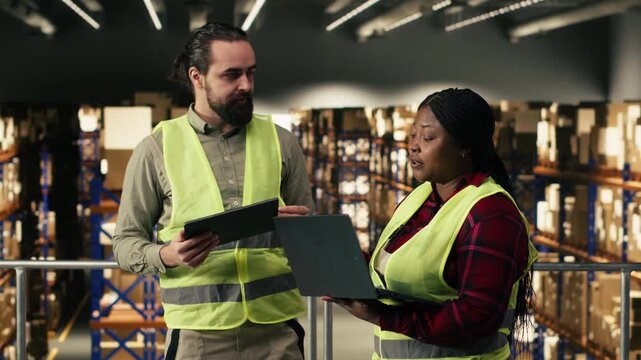 Two people working together on parcel tracking in industrial warehouse, supply chain control. Wearing safety vests, handling orders and planning shipment details for efficient operations.