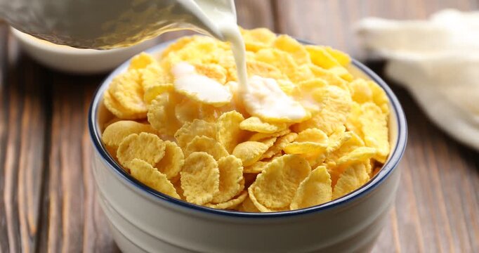 Pouring milk into bowl with corn flakes at wooden table, closeup