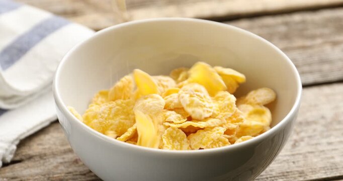 Dropping corn flakes into bowl at wooden table, closeup