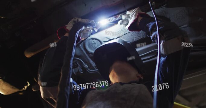 Worker wearing welding mask and gloves lighting torch under car, repairing underside in auto repair