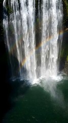 Dramatic slow motion waterfall crashing into emerald pool releasing shimmering atomized mist everywhere powerful nature