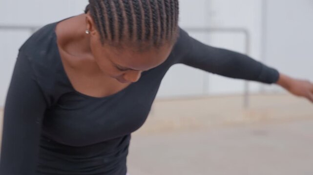 cornrows closeup showing black dancer torso leaning in slow contemporary movement, black long sleeve top, purple leggings visible, controlled breath, focused expression, rehearsal on open rooftop,