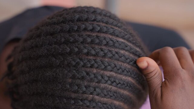 overhead black woman finishing traditional cornrows, hands smoothing ends into symmetric rows, cultural ceremony vibe, warm daylight, intimate community setting, ancestral style, care and celebration