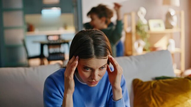 Stressed mother suffering headache active son running living room sofa closeup.