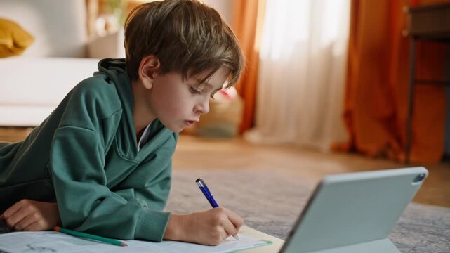 Smart pupil preparing homework browsing tablet lesson lying home floor closeup.