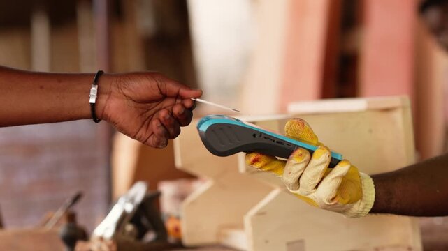 Customer making a contactless payment with credit card via POS terminal for a handcrafted wooden chair in African workshop