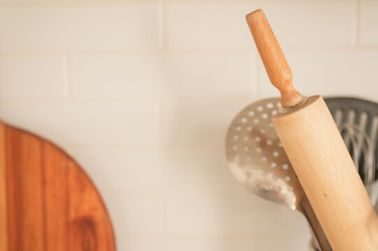 Wooden rolling pin among kitchen utensils against a white tile backsplash, with warm natural light and copy space creating a clean, cozy home cooking aesthetic