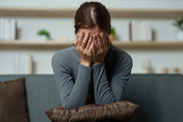 Fototapeta premium Emotional Distress. Woman covering her face in despair while sitting on a couch.