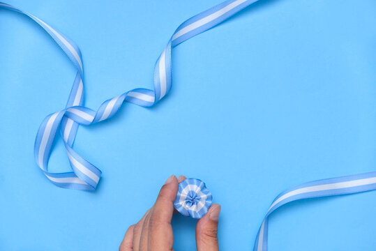 Hand holding an Argentine cockade, escarapela, on a light blue background with a national flag ribbon. Concept: celebration of national holidays.