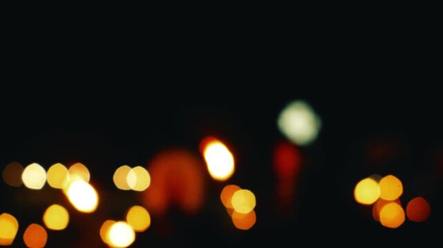 Defocused night footage of moving torchlights creating warm glowing bokeh during evening procession or public gathering.