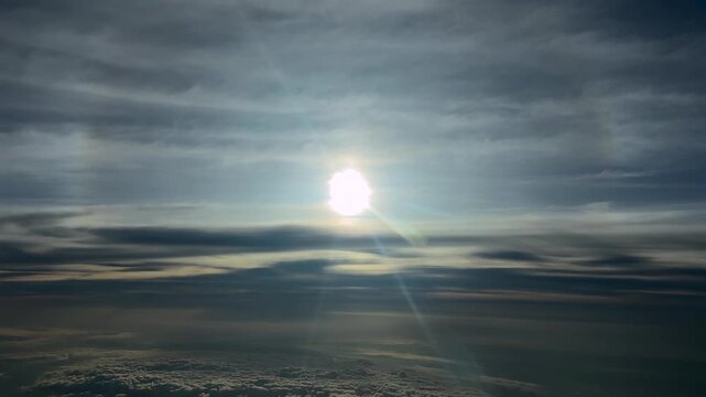 Aerial view of a glowing sun and its halo in a dramatic sky while flying in the stratosphere through layers of ethereal clouds