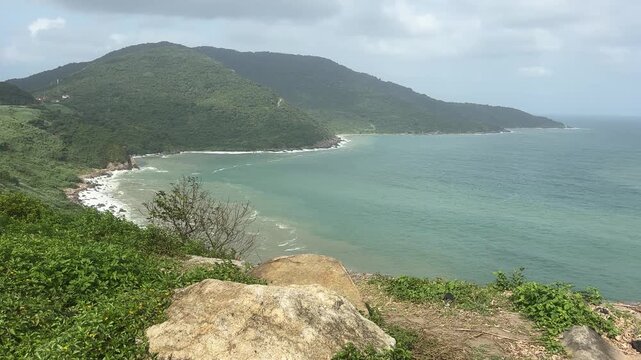 Experience a breathtaking aerial view of the Da Nang coastline, Vietnam, showcasing lush green mountains and serene blue waters. Captured with precision, this drone video captures stunning natural bea