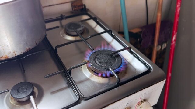 Close-up of a person igniting a gas stove burner with a handheld lighter in a domestic kitchen. Visible blue and orange flame on metal cooktop during manual ignition process.