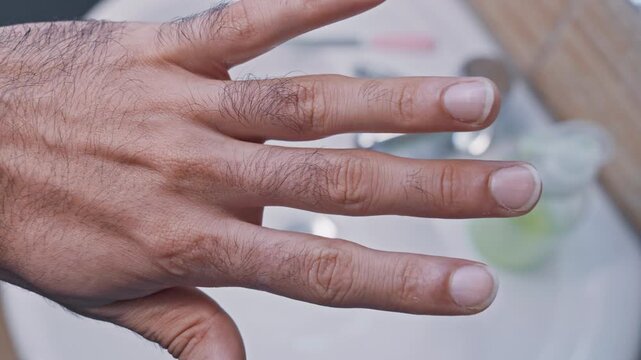 Detailed close-up view of a man's hand applying nourishing oil to his cuticles for a manicure, promoting healthy nail growth