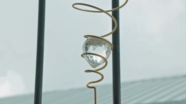 Crystal ball on a golden spiral wind spinner twisting and turning in front of a window. The faceted glass reflects light as it rotates