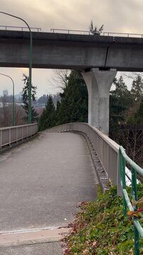 Vertical view of an empty pedestrian or bike bridge over a highway, perpendicularly underneath an overpass with cars driving by.  The concrete bridge curves downhill disappearing into view.